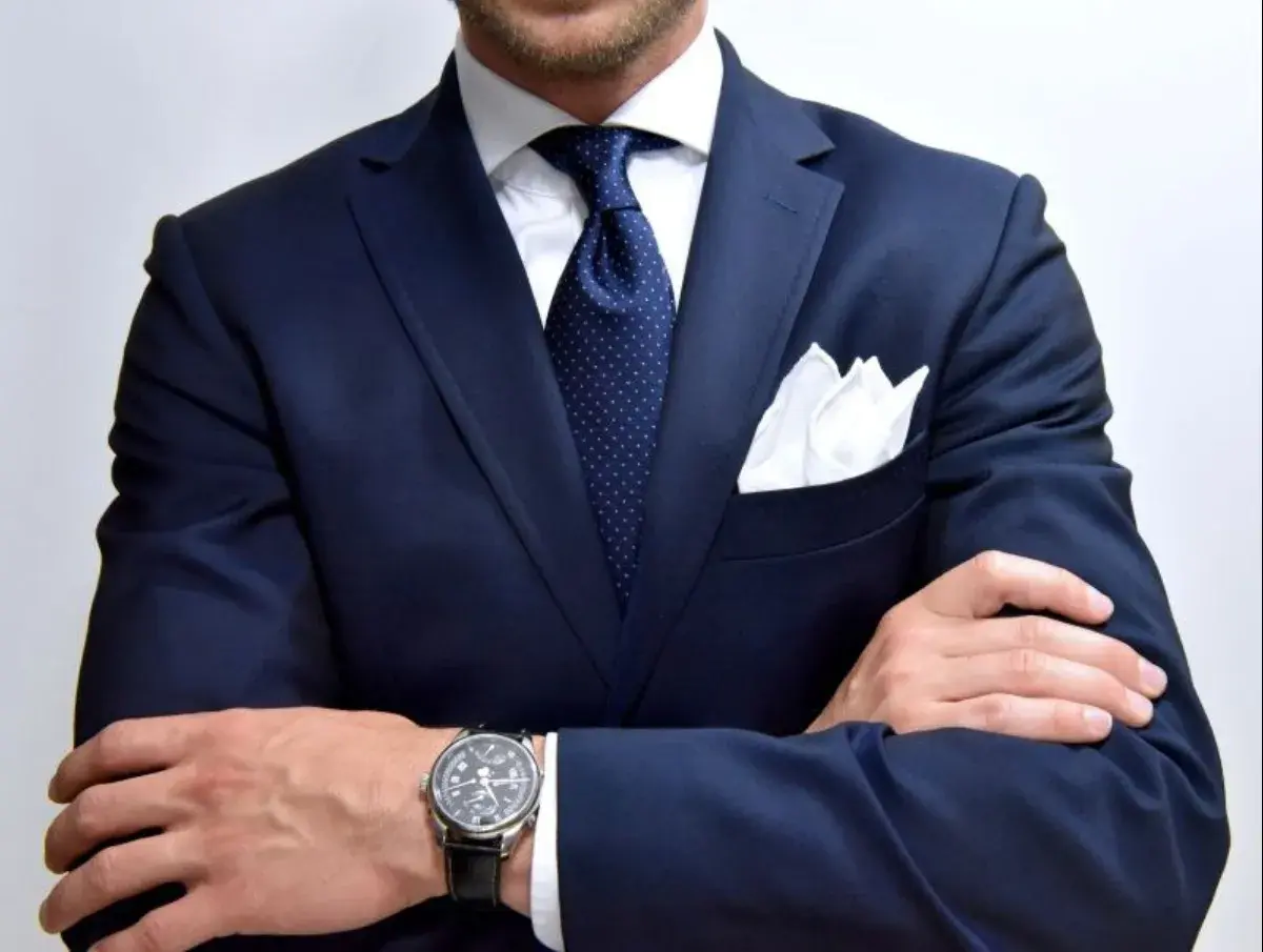 Elegancki mężczyzna w granatowym garniturze, białej koszuli i granatowym krawacie w kropki. Biała poszetka dodaje stylu. Idealny przykład, jaki krawat do granatowego garnituru.