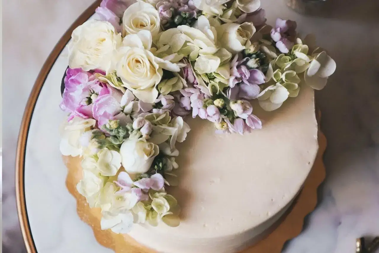 Delikatny tort ozdobiony bukietem pastelowych, jakie żywe kwiaty na tort – róże, hortensje i niezapominajki.