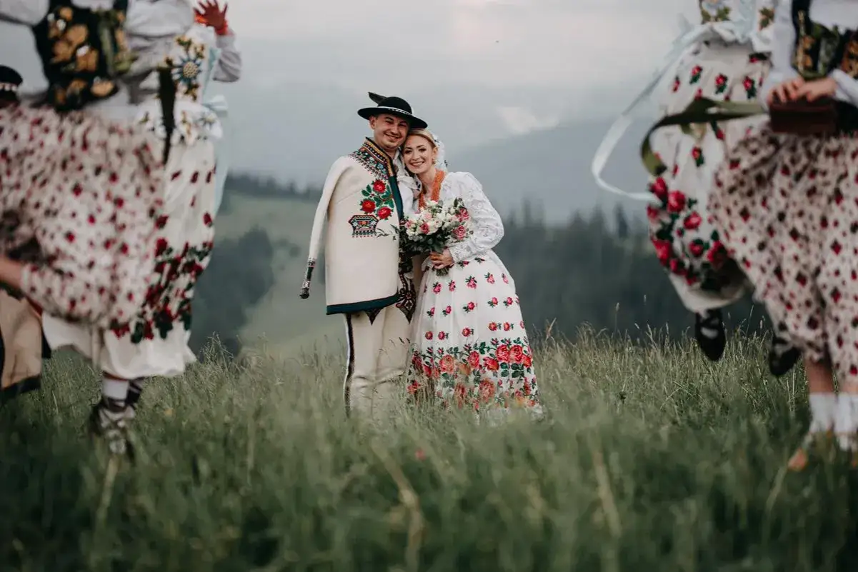 Para młoda w strojach ludowych, otoczona przez tańczące zespoły góralskie.