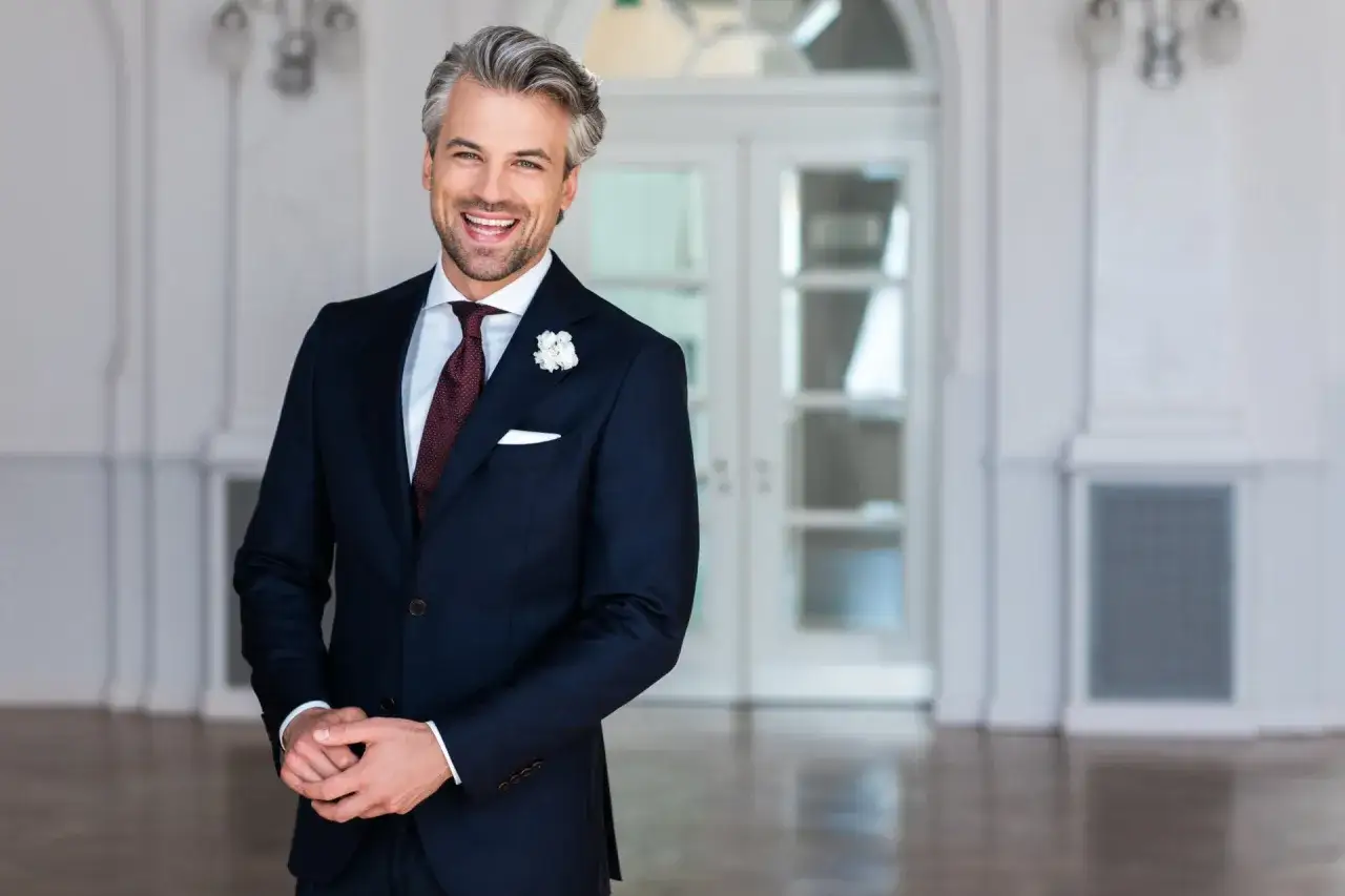 Elegancki mężczyzna w granatowym garniturze, białej koszuli i bordowym krawacie, idealny przykład, jaka koszula do granatowego garnituru na wesele.
