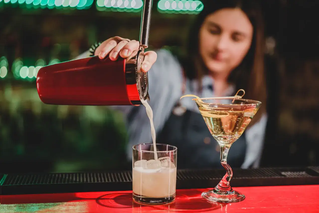 Barman przygotowuje drinki na wieczór panieński. Czerwony shaker i kieliszek martini z cytrynową skórką.