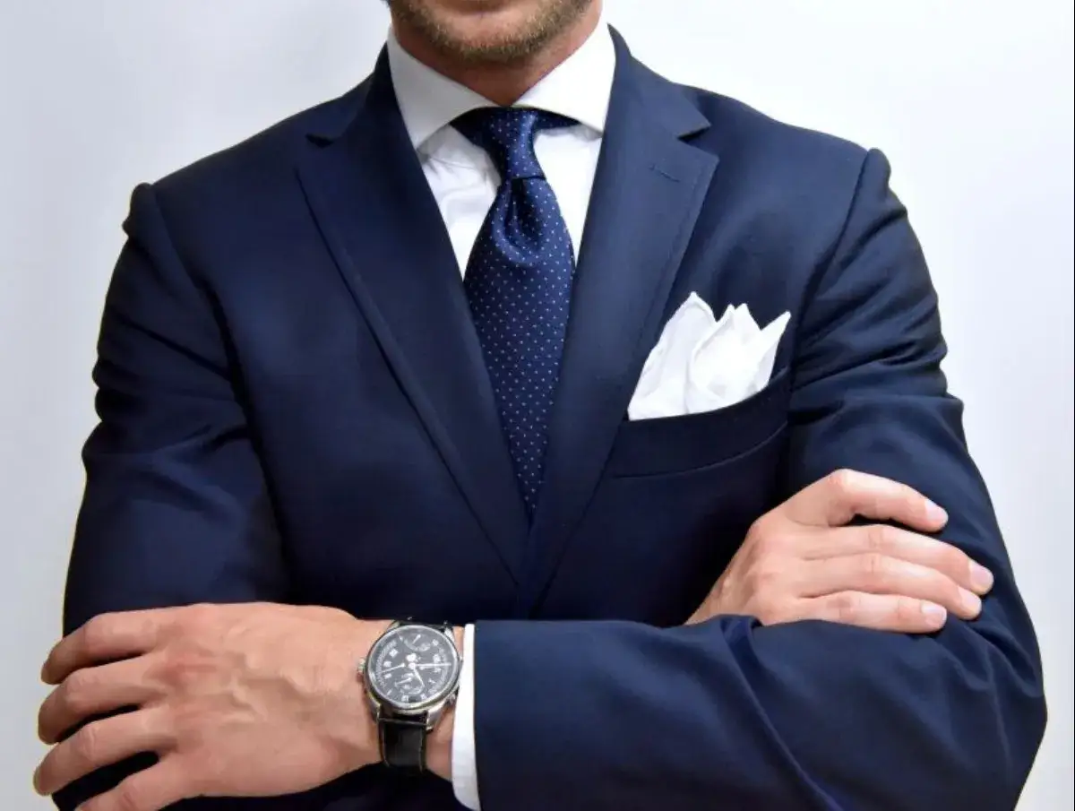 Elegancki mężczyzna w granatowym garniturze, z białą poszetką i granatowym krawatem w kropki. Idealna inspiracja, jaki krawat do granatowego garnituru.